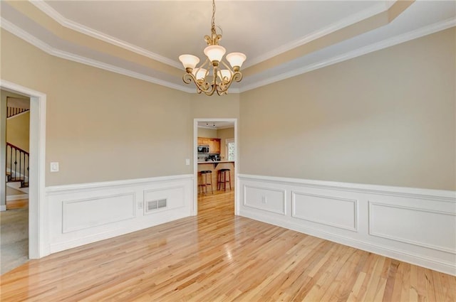 39 Legendary Dr, Hoschton, GA 30548 - empty room featuring a chandelier, light wood finished floors, a raised ceiling, ornamental molding, and a wainscoted wall