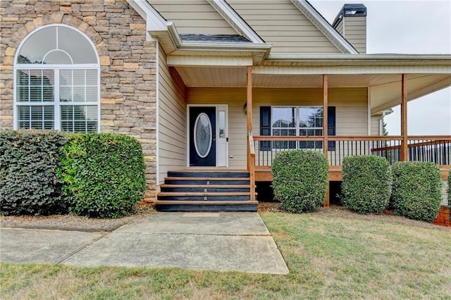 39 Legendary Dr, Hoschton, GA 30548 - view of exterior entry with stone siding, a porch, a chimney, and a lawn