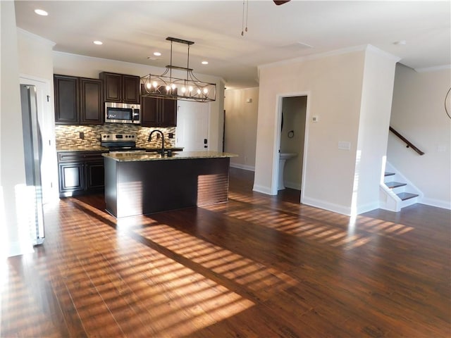 kitchen with light stone counters, stainless steel appliances, dark wood-type flooring, backsplash, and an island with sink