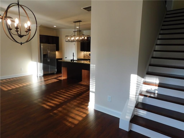 staircase featuring a chandelier, visible vents, baseboards, and wood finished floors