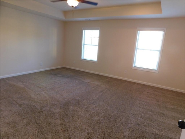 carpeted empty room with a tray ceiling, ceiling fan, and baseboards