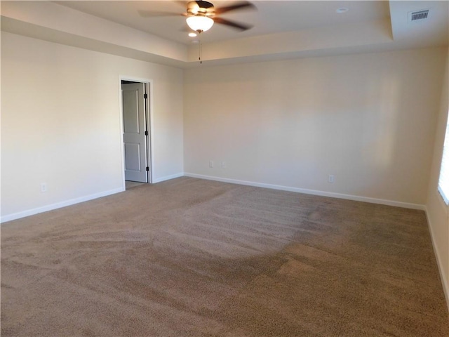 unfurnished room featuring ceiling fan, a tray ceiling, visible vents, and baseboards