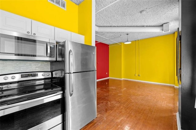 kitchen featuring a textured ceiling, hardwood / wood-style floors, appliances with stainless steel finishes, white cabinets, and tasteful backsplash