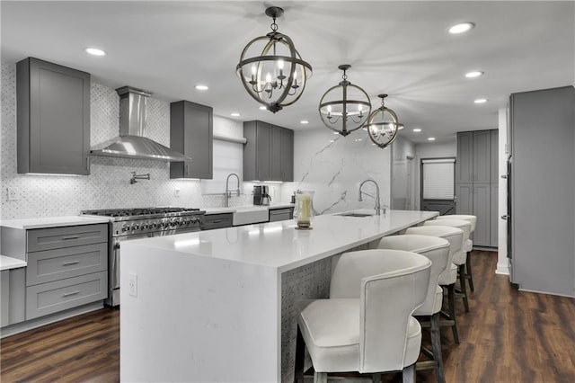 kitchen featuring high end stainless steel range, decorative light fixtures, a center island with sink, dark hardwood / wood-style flooring, and wall chimney range hood