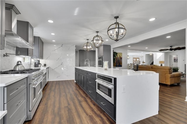 kitchen with appliances with stainless steel finishes, decorative light fixtures, sink, dark wood-type flooring, and a center island with sink