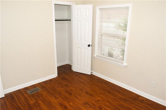 unfurnished bedroom with a closet, dark hardwood / wood-style floors, and multiple windows