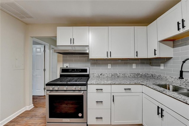 kitchen with decorative backsplash, sink, white cabinetry, stainless steel gas stove, and light stone counters