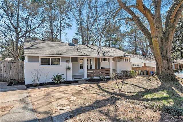 ranch-style house with covered porch, brick siding, fence, and a chimney