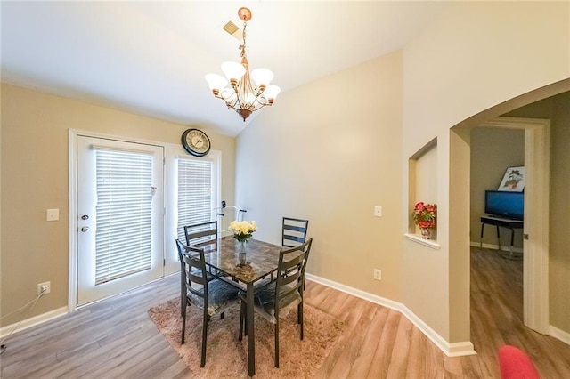 dining space with a chandelier, light wood-type flooring, lofted ceiling, and baseboards