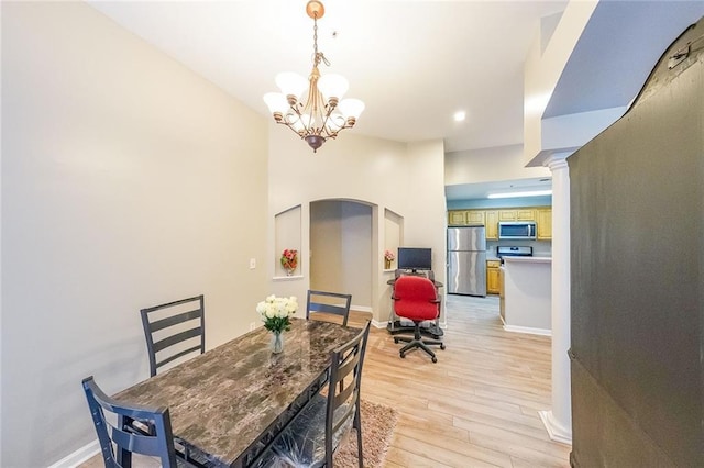 dining area with baseboards, light wood-type flooring, arched walkways, and an inviting chandelier