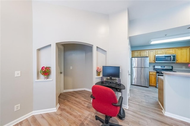 kitchen with arched walkways, light countertops, appliances with stainless steel finishes, light wood-style floors, and baseboards