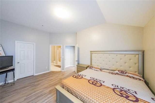 bedroom featuring lofted ceiling, ensuite bathroom, light wood-style flooring, and baseboards