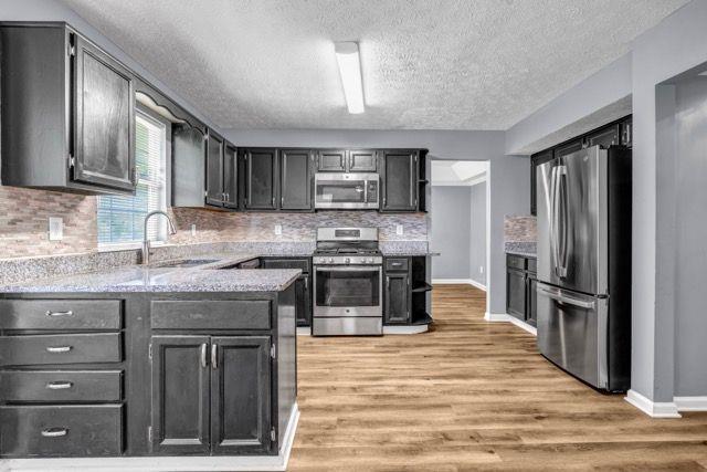 2505 Tiffany Ct SE, Conyers, GA 30013 - kitchen with stainless steel appliances, a sink, light wood finished floors, a textured ceiling, and decorative backsplash