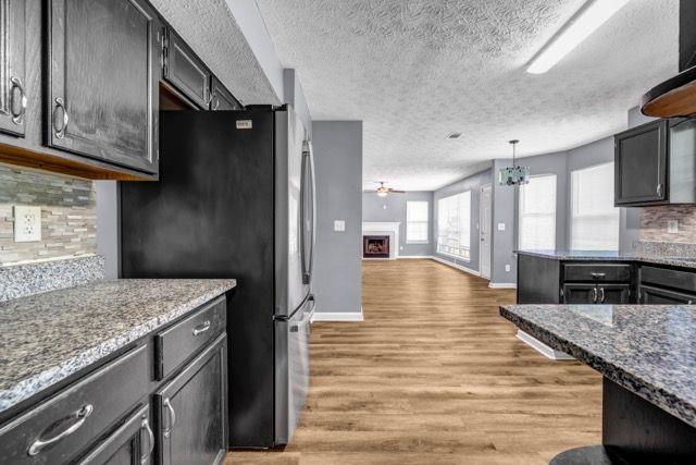 2505 Tiffany Ct SE, Conyers, GA 30013 - kitchen featuring freestanding refrigerator, a textured ceiling, tasteful backsplash, light wood finished floors, and a fireplace