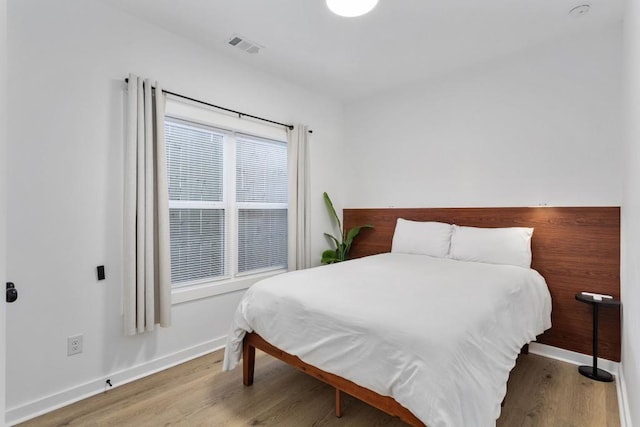 bedroom with wood finished floors, visible vents, and baseboards