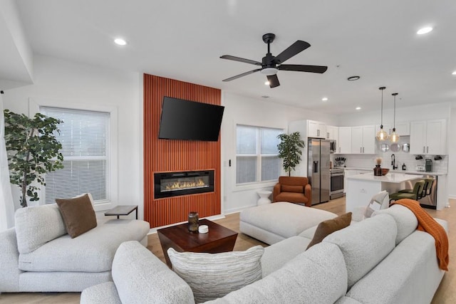 living area with light wood-style flooring, ceiling fan, a glass covered fireplace, and recessed lighting