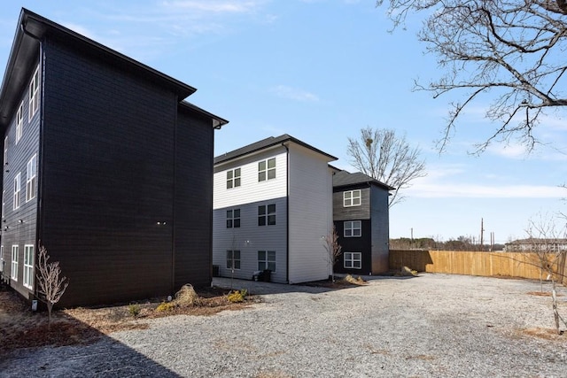 view of side of home featuring gravel driveway and fence