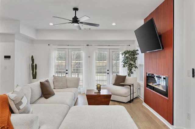 living area with french doors, light wood-type flooring, a glass covered fireplace, and recessed lighting