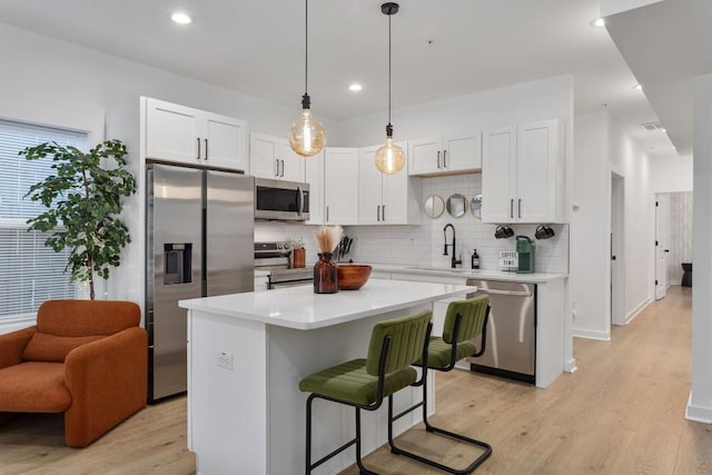 kitchen featuring a kitchen island, a sink, white cabinetry, light countertops, and appliances with stainless steel finishes