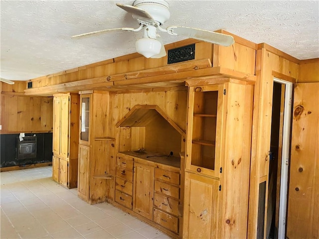 interior space featuring a textured ceiling, ceiling fan, a wood stove, and wooden walls