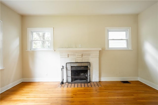 unfurnished living room featuring a healthy amount of sunlight, a tile fireplace, and light hardwood / wood-style floors