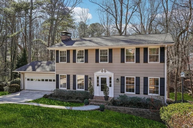 colonial home featuring an attached garage, driveway, a chimney, and a front yard