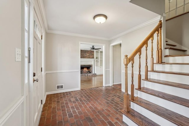 entrance foyer with brick floor, a fireplace, baseboards, stairs, and ornamental molding