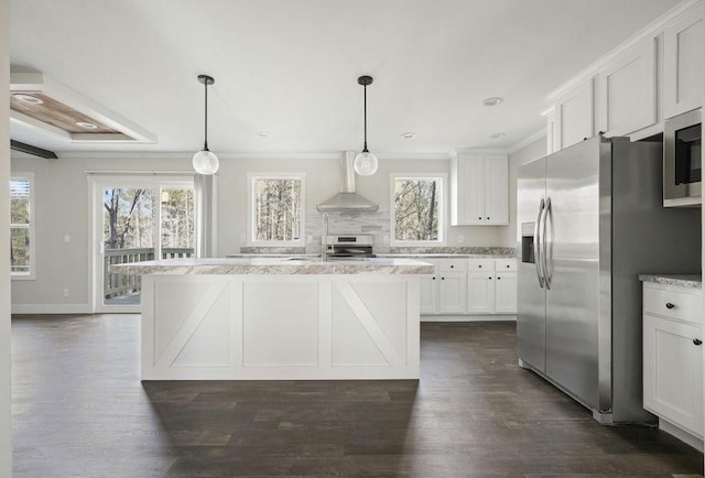 kitchen with decorative light fixtures, wall chimney range hood, a kitchen island, appliances with stainless steel finishes, and white cabinets