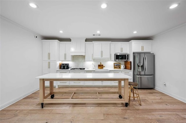 kitchen with backsplash, stainless steel appliances, ornamental molding, and white cabinetry