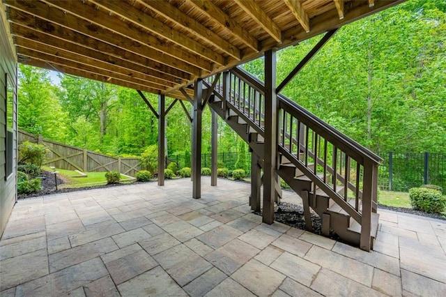 view of patio / terrace featuring a forest view, stairs, and a fenced backyard