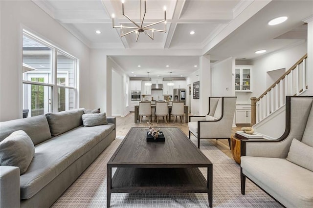 living room with beam ceiling, an inviting chandelier, ornamental molding, coffered ceiling, and stairs