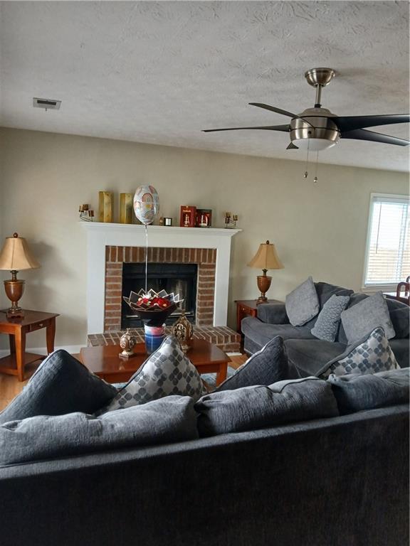 living room featuring a ceiling fan, wood finished floors, visible vents, a fireplace, and a textured ceiling