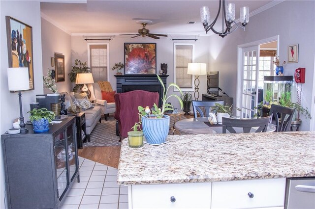 interior space featuring light wood-type flooring, light stone counters, ceiling fan with notable chandelier, crown molding, and white cabinets