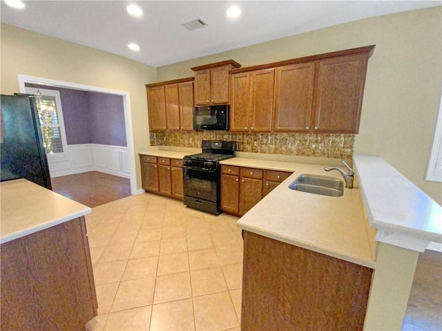 kitchen featuring brown cabinets, a peninsula, light countertops, black appliances, and a sink