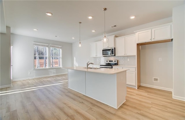 kitchen featuring appliances with stainless steel finishes, decorative light fixtures, sink, white cabinets, and a kitchen island with sink