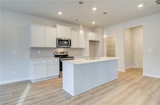 kitchen with white cabinets, stainless steel appliances, light hardwood / wood-style floors, hanging light fixtures, and a center island with sink