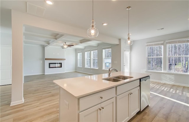 kitchen with beamed ceiling, white cabinetry, a kitchen island with sink, stainless steel dishwasher, and sink