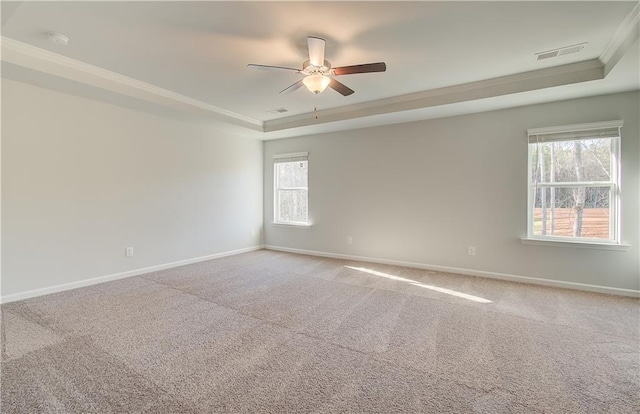 carpeted spare room featuring ceiling fan, crown molding, a raised ceiling, and a healthy amount of sunlight