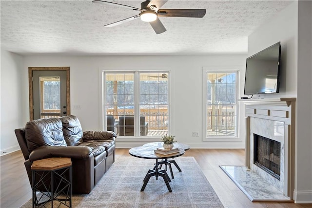 living room featuring a high end fireplace, wood-type flooring, a textured ceiling, and ceiling fan