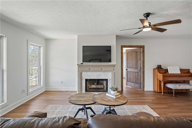 living room with a high end fireplace, a textured ceiling, ceiling fan, and light hardwood / wood-style floors