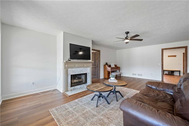 living room featuring a high end fireplace, a textured ceiling, ceiling fan, and hardwood / wood-style floors