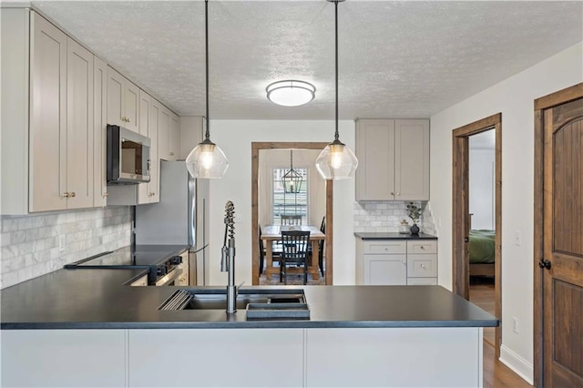 kitchen with decorative light fixtures, stainless steel appliances, a textured ceiling, and tasteful backsplash