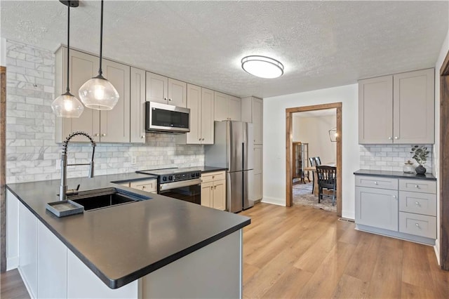 kitchen with appliances with stainless steel finishes, hanging light fixtures, kitchen peninsula, sink, and light hardwood / wood-style flooring