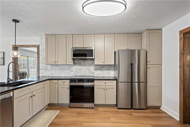 kitchen with hanging light fixtures, light hardwood / wood-style floors, backsplash, appliances with stainless steel finishes, and sink