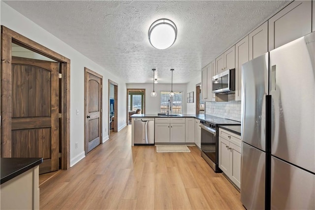 kitchen featuring stainless steel appliances, sink, tasteful backsplash, kitchen peninsula, and pendant lighting