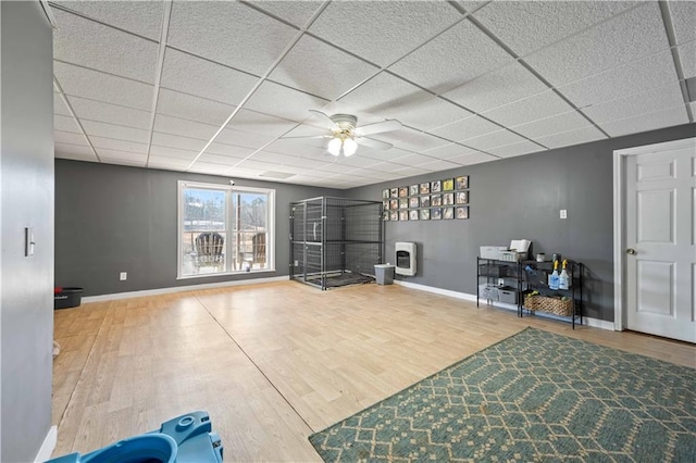 workout area with a drop ceiling, ceiling fan, heating unit, and hardwood / wood-style floors