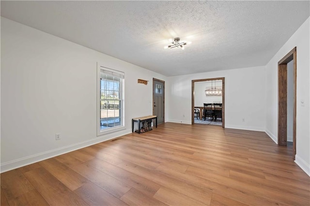 unfurnished living room featuring a textured ceiling, light wood-type flooring, and an inviting chandelier