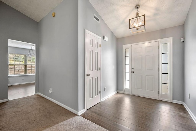 foyer entrance with lofted ceiling, visible vents, an inviting chandelier, wood finished floors, and baseboards