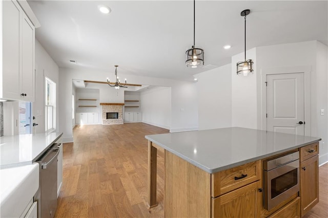 kitchen with hanging light fixtures, light wood-style flooring, a brick fireplace, and stainless steel appliances