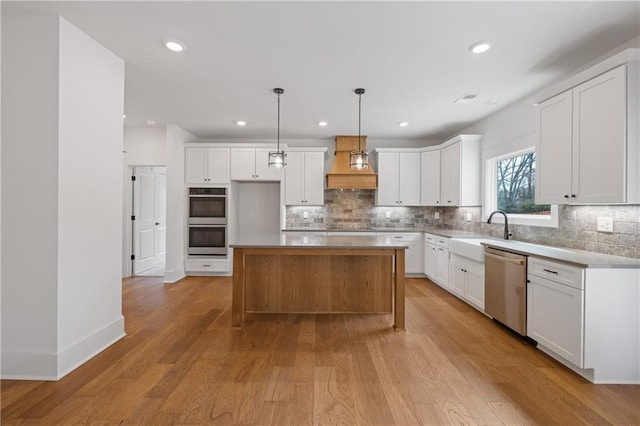 kitchen featuring light wood finished floors, custom exhaust hood, a sink, stainless steel appliances, and tasteful backsplash